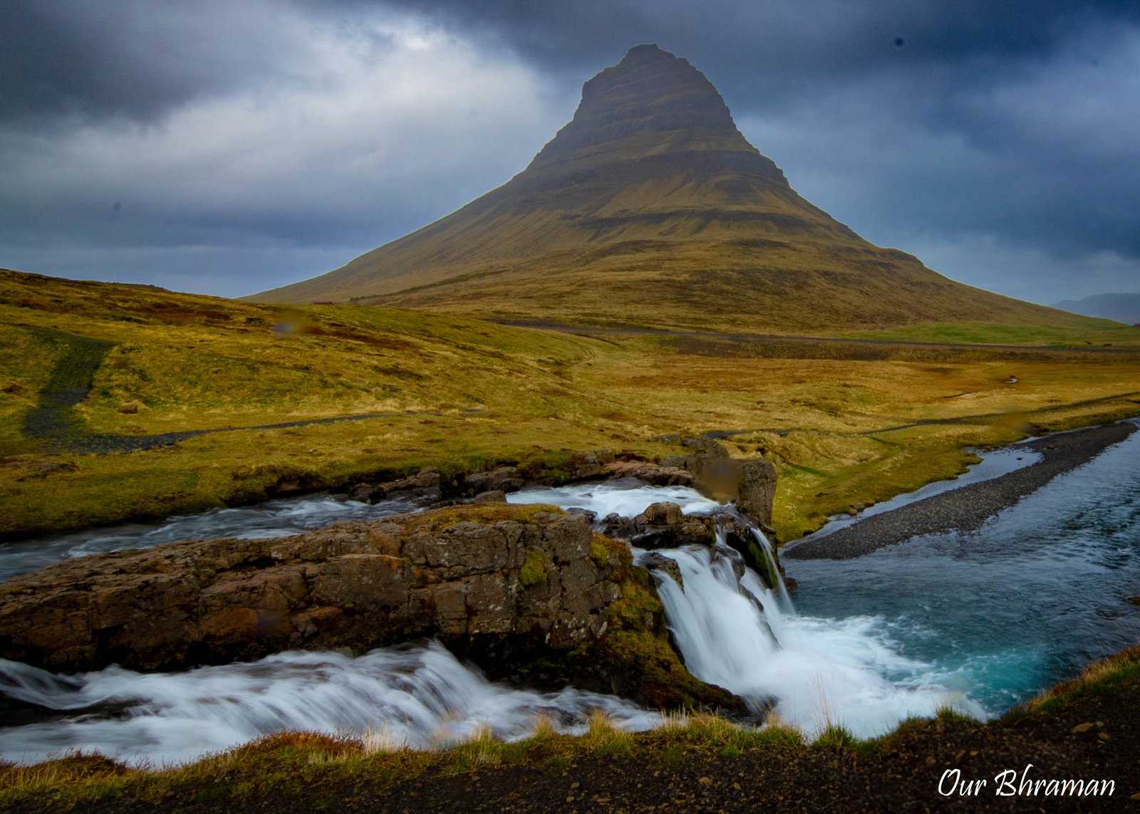 The iconic cone-shaped Kirkjufell mountain towers over the multi-tiered Kirkjufellsfoss waterfall