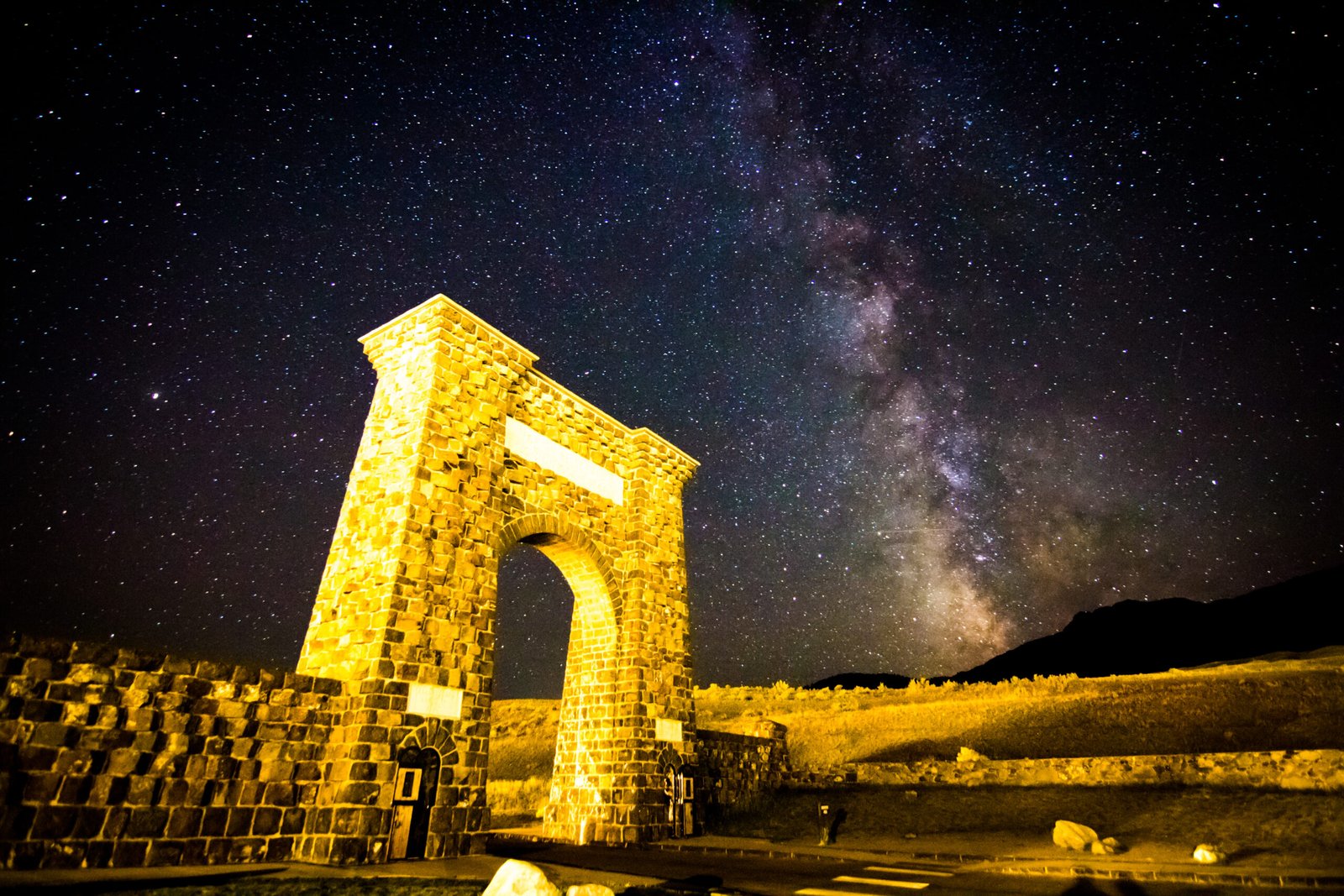 The historic stone Roosevelt Arch under the starry Milky Way galaxy sky at the North Entrance of Yellowstone National Park.