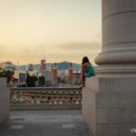 View of Plaça d'Espanya in Barcelona, Spain, framed by large stone columns looking out toward the city skyline and the distant Tibidabo Mountain.