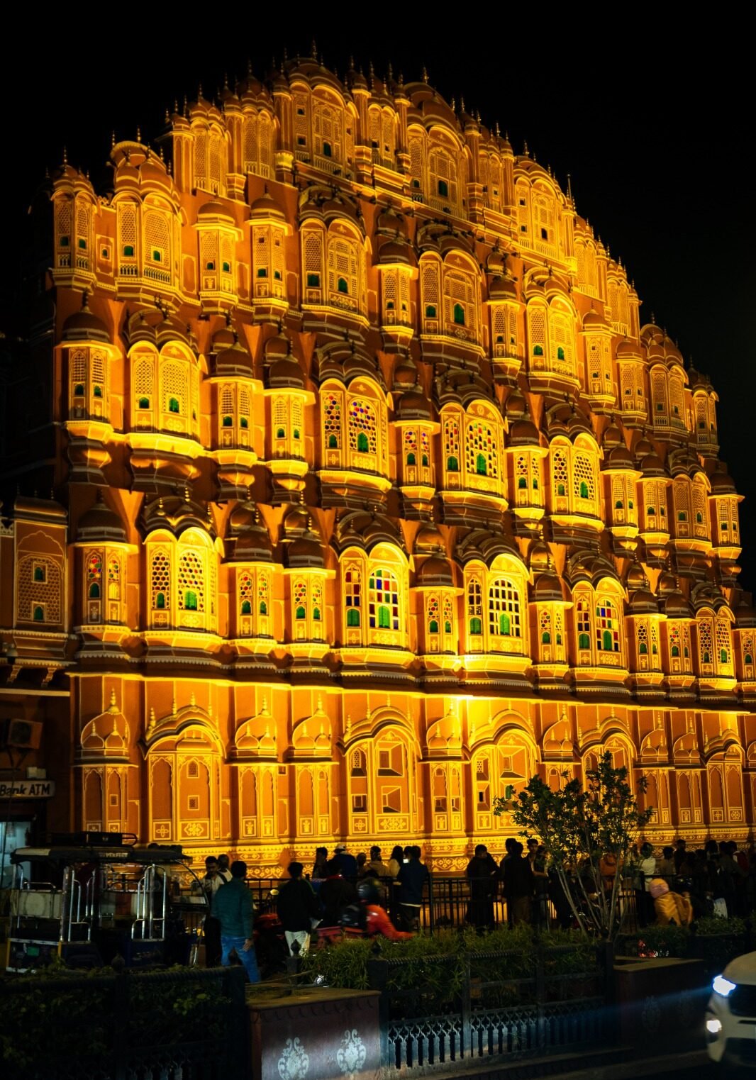The massive, intricately carved red and pink sandstone facade of the Hawa Mahal (Palace of Winds) stands grandly illuminated by warm golden lights at night in Jaipur, India.